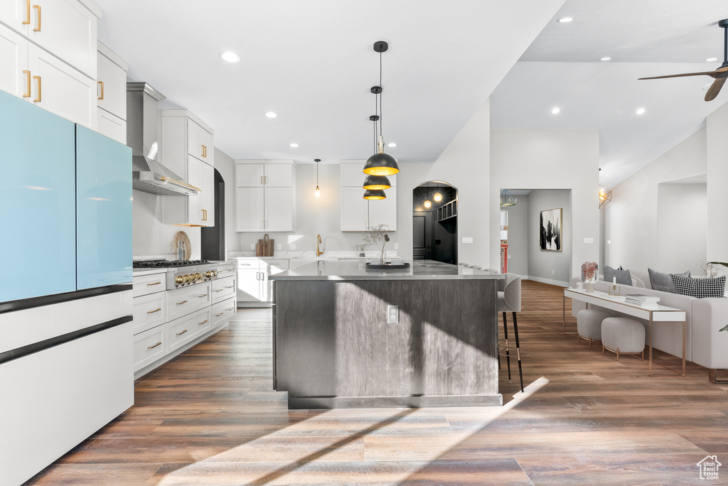 Kitchen with freestanding refrigerator, wall chimney range hood, ceiling fan, a kitchen island with sink, and recessed lighting