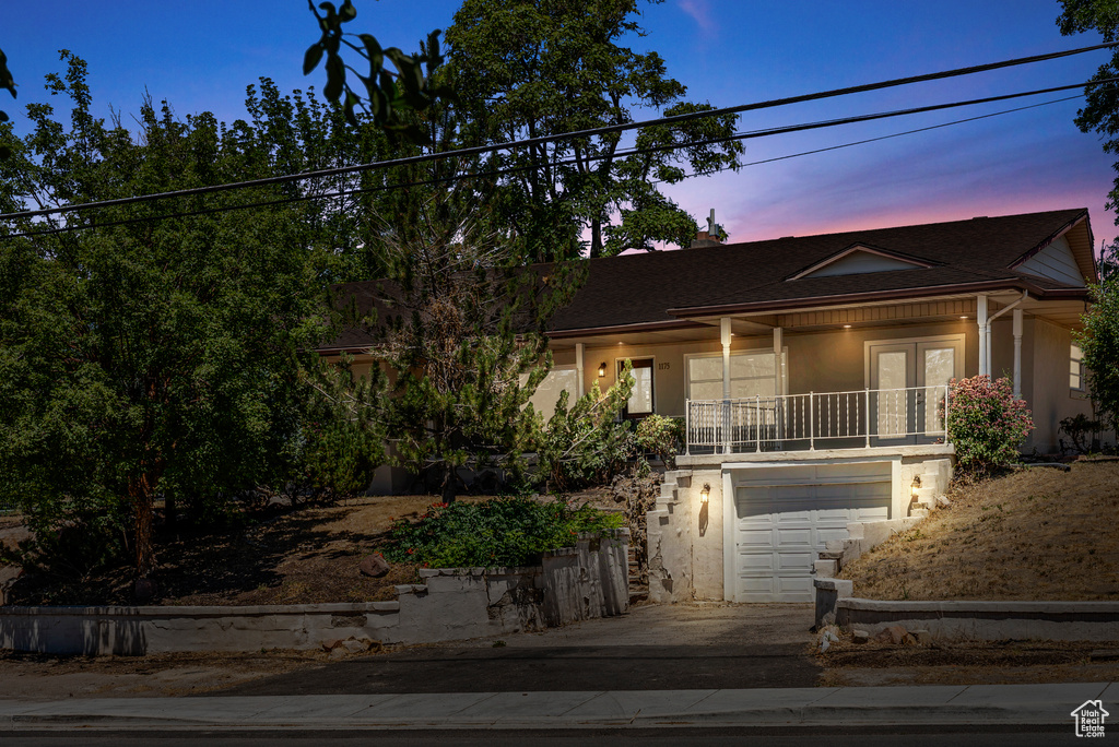 View of front facade featuring french doors, stucco siding, an attached garage, and driveway