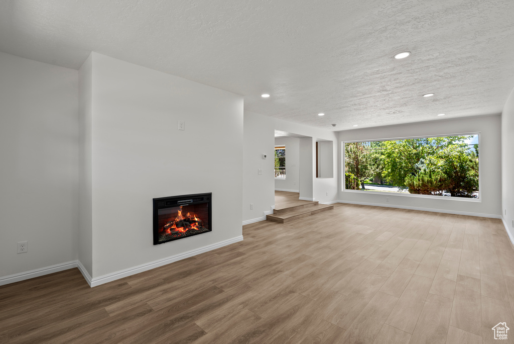 Unfurnished living room featuring recessed lighting, wood finished floors, a glass covered fireplace, and a textured ceiling