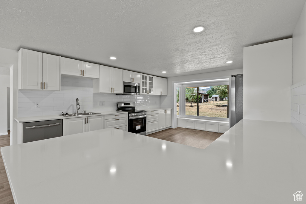 Kitchen featuring stainless steel appliances, wood finished floors, white cabinetry, light countertops, and tasteful backsplash