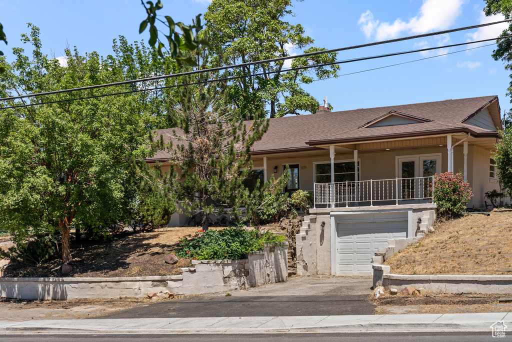 View of front of house with an attached garage, french doors, driveway, roof with shingles, and stucco siding