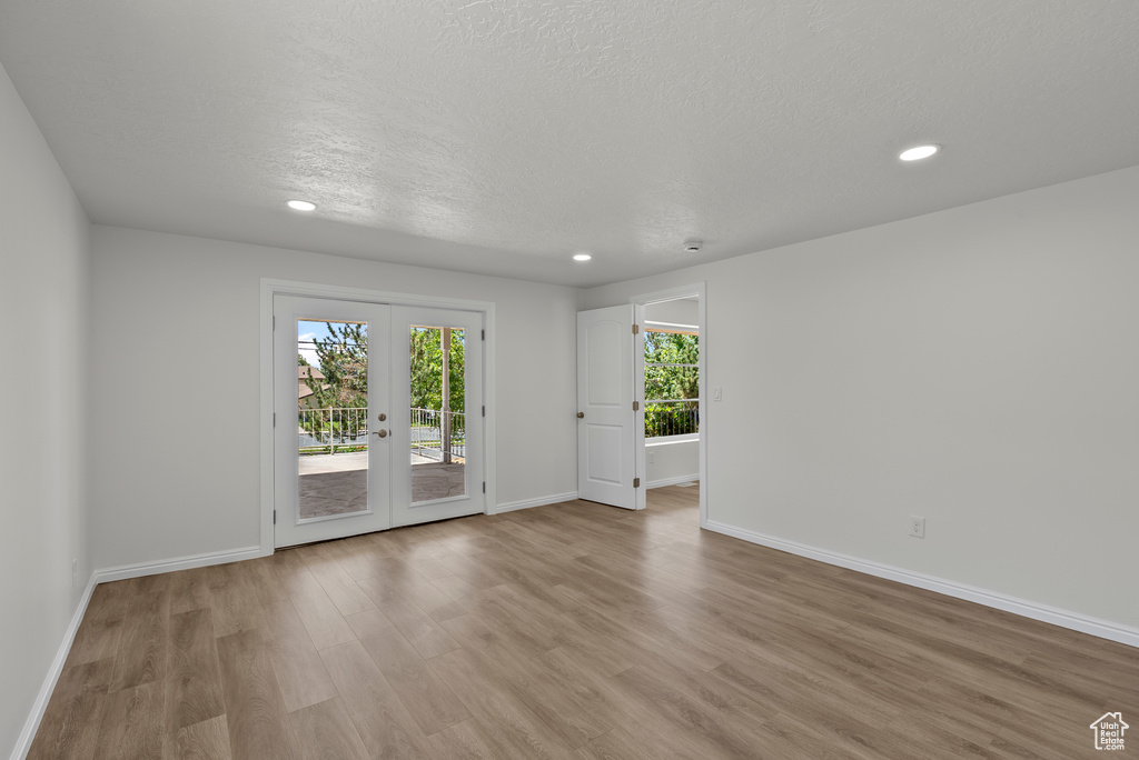 Unfurnished room featuring french doors, light wood-type flooring, recessed lighting, and a textured ceiling