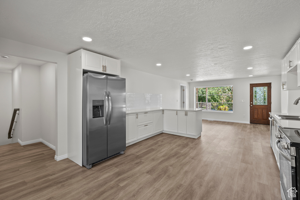 Kitchen featuring appliances with stainless steel finishes, recessed lighting, light wood-style floors, a peninsula, and white cabinets