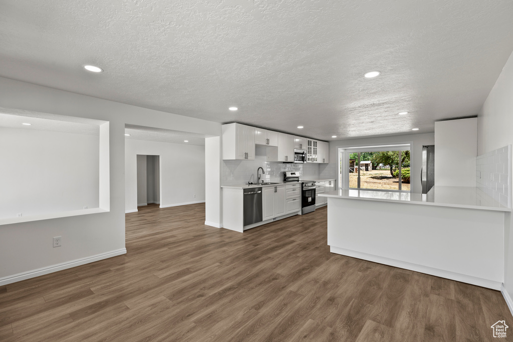 Kitchen featuring appliances with stainless steel finishes, light countertops, white cabinets, wood finished floors, and recessed lighting