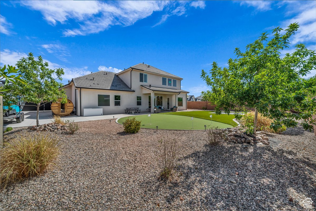 Rear view of house with an area to practice putting, a patio, stucco siding, and a fenced backyard