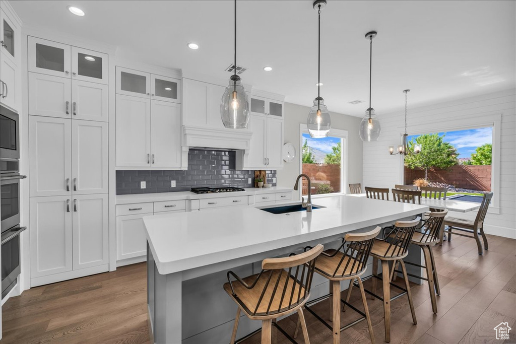 Kitchen with wood finished floors, a kitchen island with sink, a breakfast bar, decorative backsplash, and light countertops