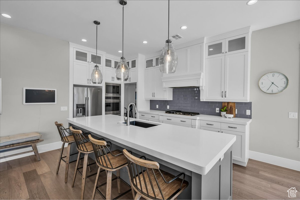 Kitchen with stainless steel appliances, wood finished floors, tasteful backsplash, a kitchen island with sink, and a kitchen bar
