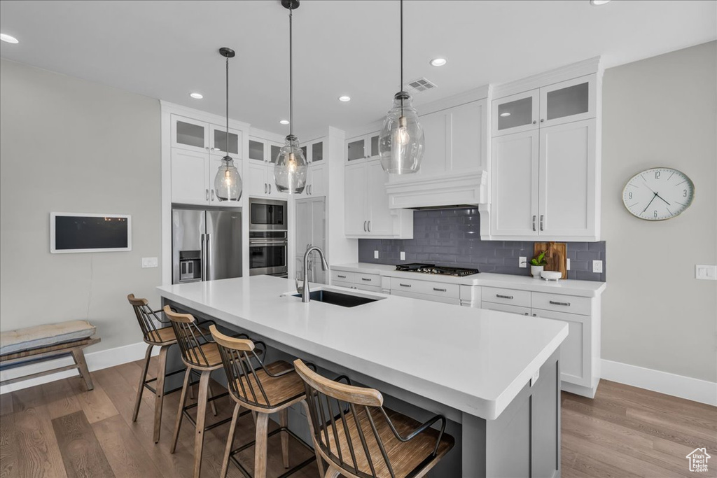 Kitchen featuring appliances with stainless steel finishes, dark wood-style floors, decorative backsplash, an island with sink, and white cabinetry