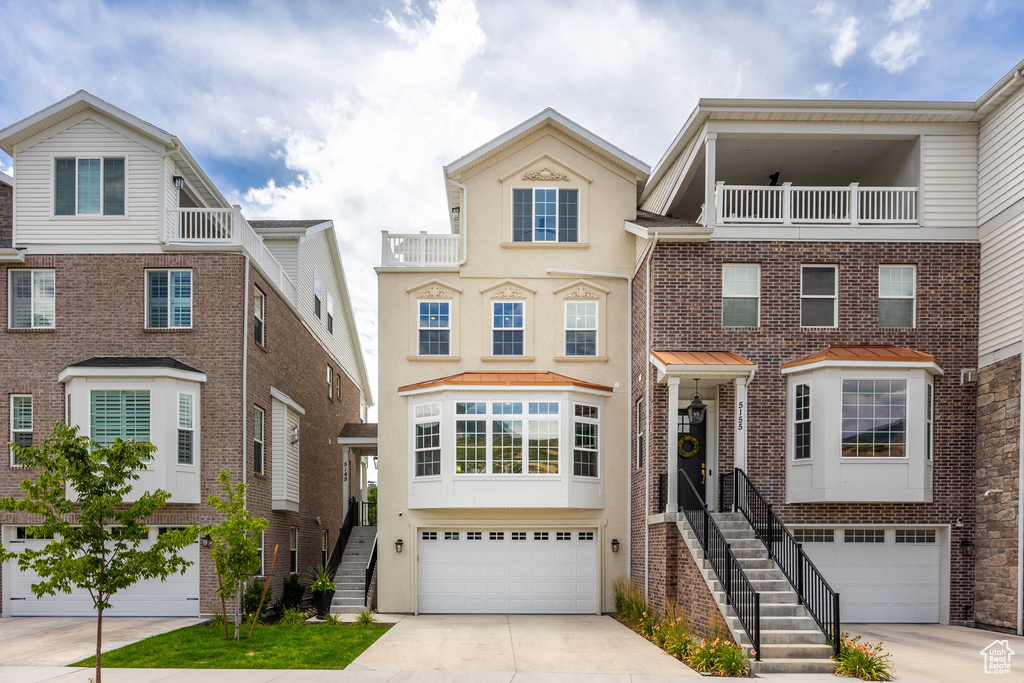View of front of property featuring concrete driveway, stairs, an attached garage, and a balcony