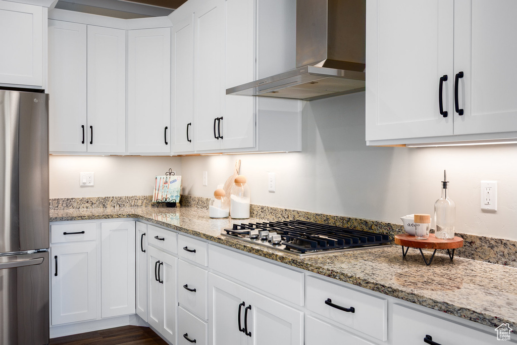 Kitchen with wall chimney range hood, appliances with stainless steel finishes, white cabinets, and light stone countertops