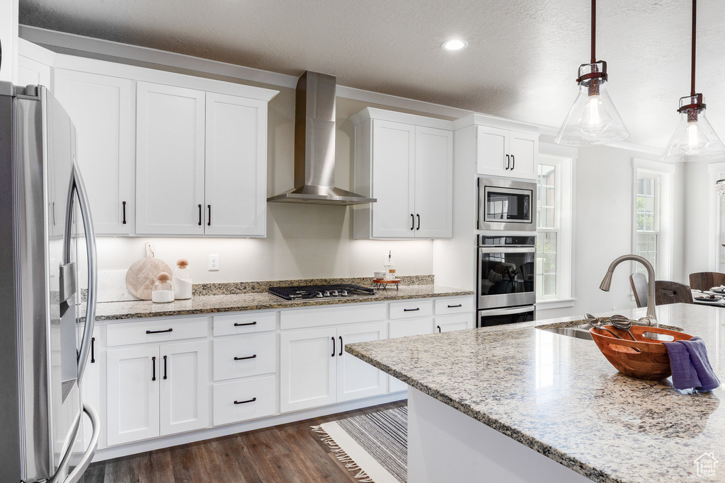 Kitchen featuring stainless steel appliances, wall chimney exhaust hood, dark wood-type flooring, white cabinetry, and light stone countertops