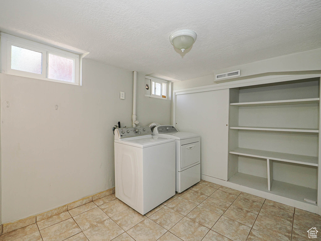 Laundry area with independent washer and dryer, a textured ceiling, and light tile patterned floors