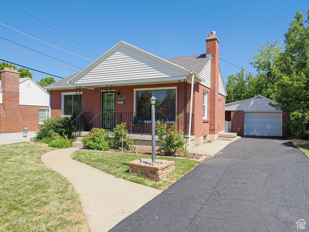 View of front of property with brick siding, an outdoor structure, a chimney, a detached garage, and a front lawn