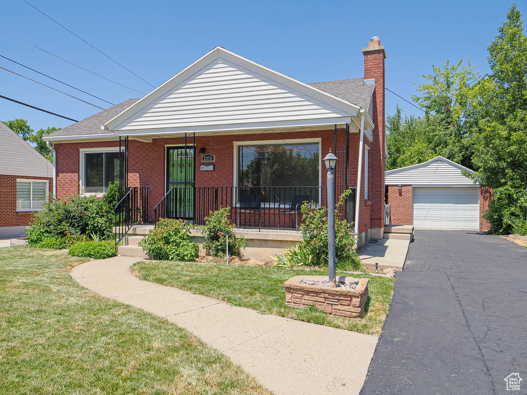 Bungalow featuring an outdoor structure, a front yard, a chimney, and brick siding