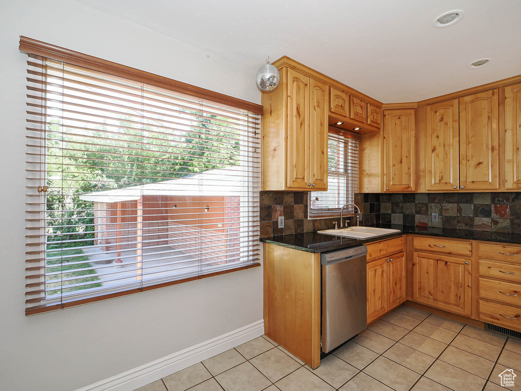 Kitchen featuring stainless steel dishwasher, light tile patterned floors, backsplash, and dark countertops
