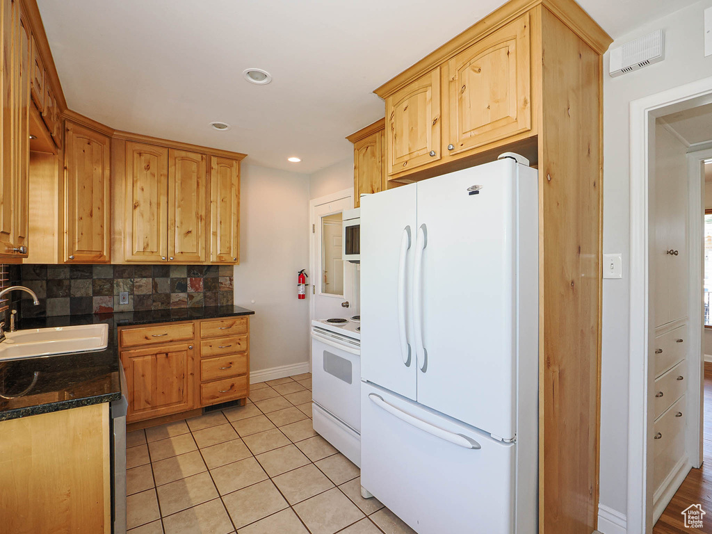 Kitchen with white appliances, dark countertops, tasteful backsplash, light brown cabinetry, and recessed lighting