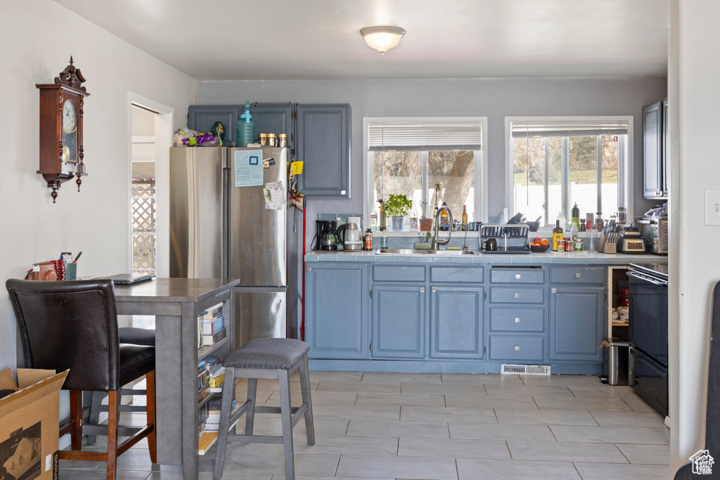 Kitchen with freestanding refrigerator, tile countertops, blue cabinetry, and stove