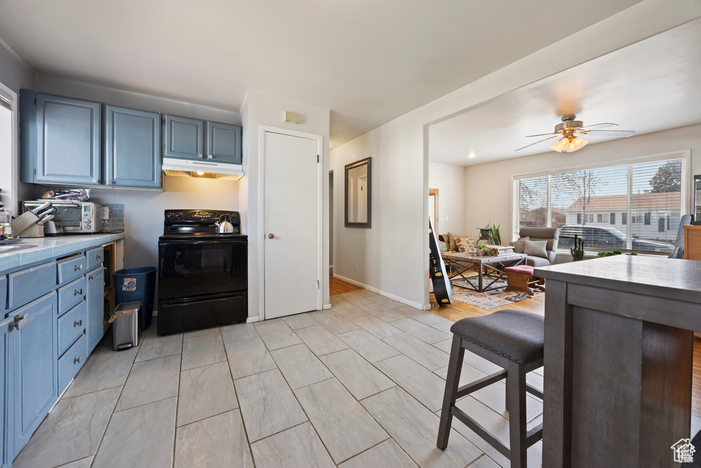 Kitchen featuring electric range, under cabinet range hood, blue cabinets, tile counters, and a kitchen bar