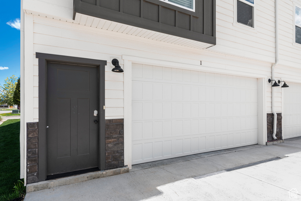 View of exterior entry featuring a garage, stone siding, and concrete driveway
