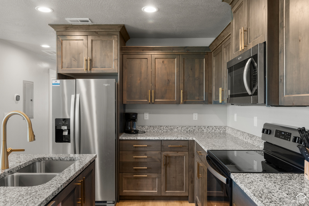 Kitchen featuring appliances with stainless steel finishes, electric panel, light stone countertops, recessed lighting, and dark brown cabinetry