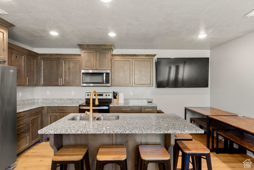 Kitchen featuring stainless steel appliances, light wood finished floors, a breakfast bar, recessed lighting, and a textured ceiling