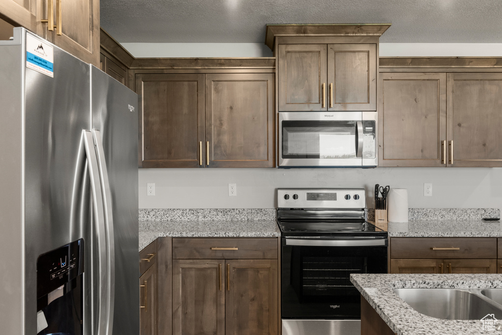 Kitchen with stainless steel appliances, a textured ceiling, and light stone countertops