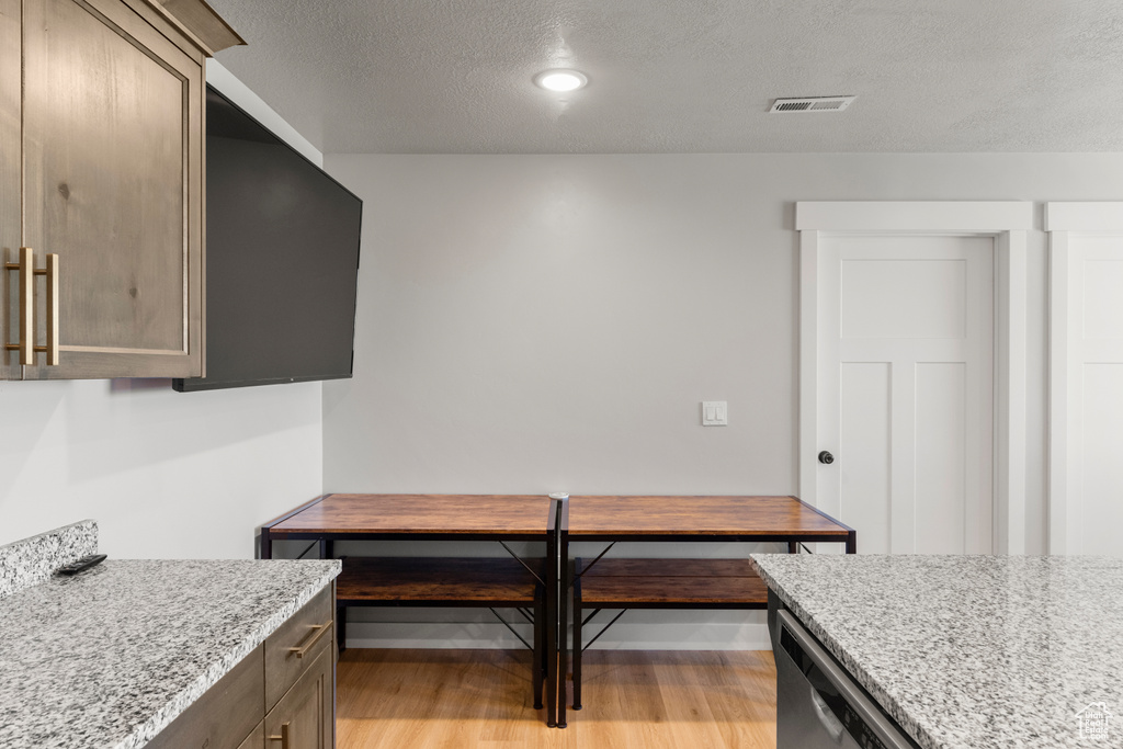 Kitchen with a textured ceiling, light stone countertops, light wood-style flooring, recessed lighting, and stainless steel dishwasher