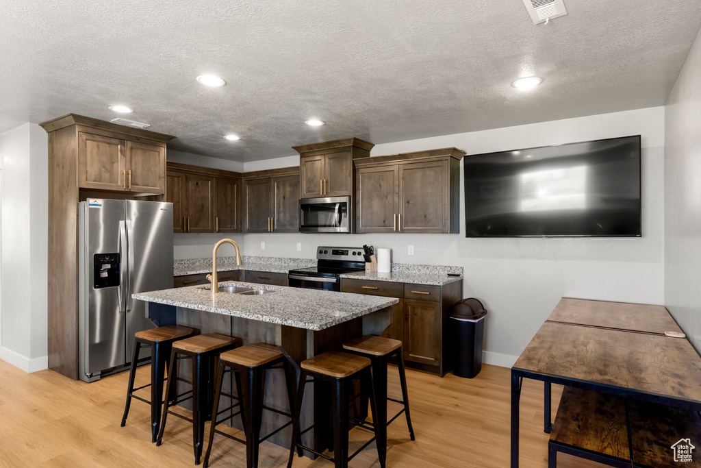 Kitchen with stainless steel appliances, light stone countertops, light wood-style flooring, a textured ceiling, and recessed lighting