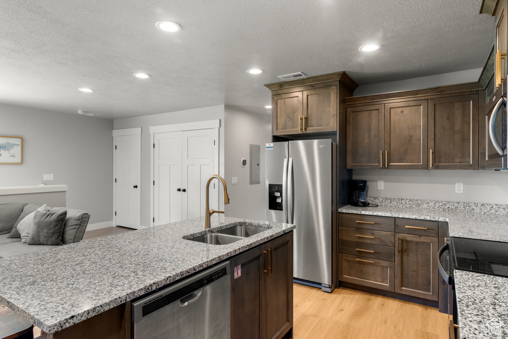 Kitchen featuring stainless steel appliances, recessed lighting, a center island with sink, a textured ceiling, and light wood finished floors