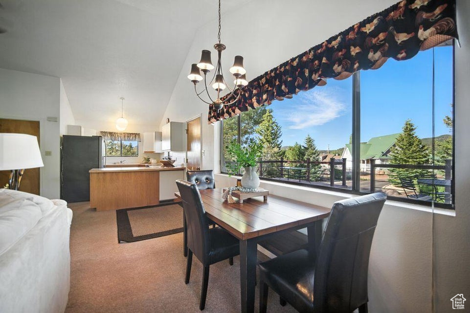 Dining area with a chandelier, light colored carpet, and vaulted ceiling