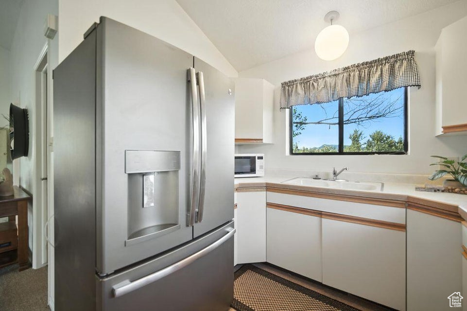 Kitchen featuring stainless steel fridge with ice dispenser, white cabinetry, white microwave, vaulted ceiling, and light countertops