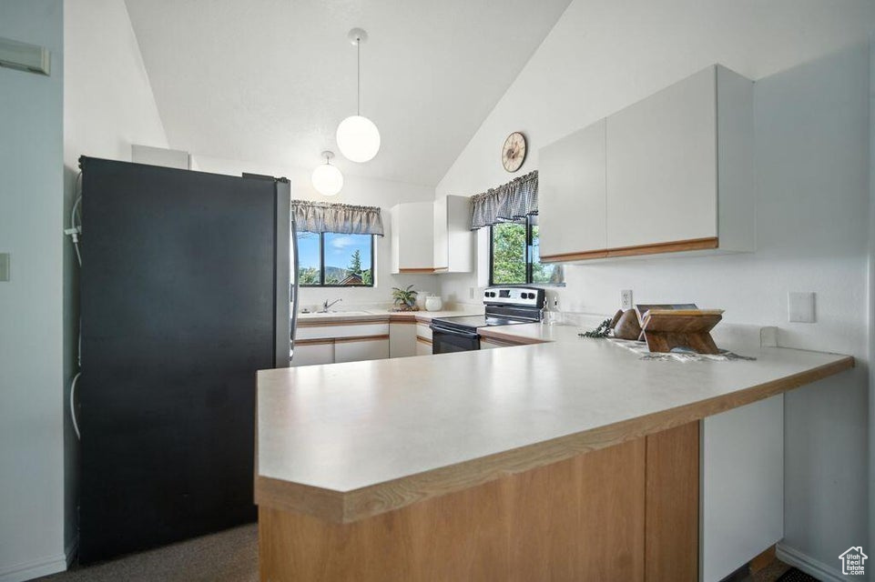 Kitchen featuring electric range oven, freestanding refrigerator, a peninsula, light countertops, and vaulted ceiling