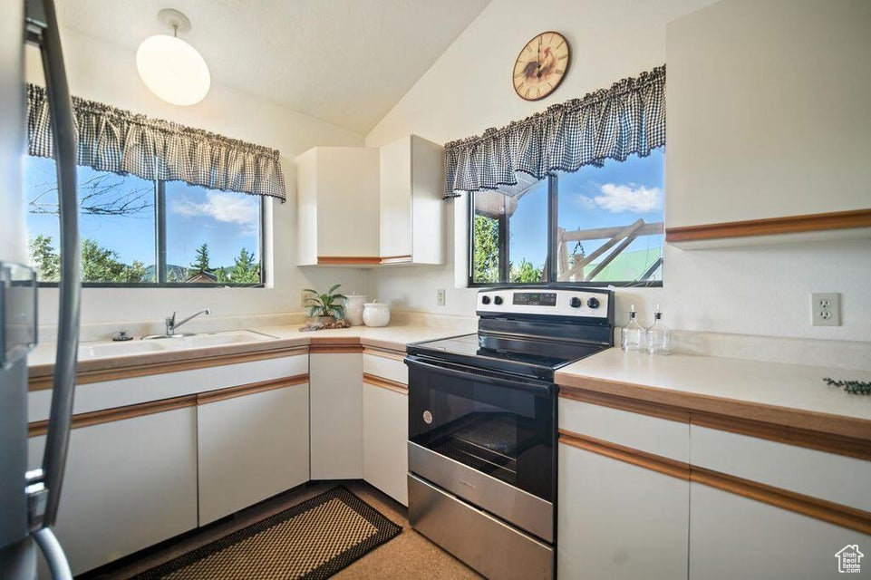 Kitchen featuring stainless steel electric stove, vaulted ceiling, white cabinets, and light countertops