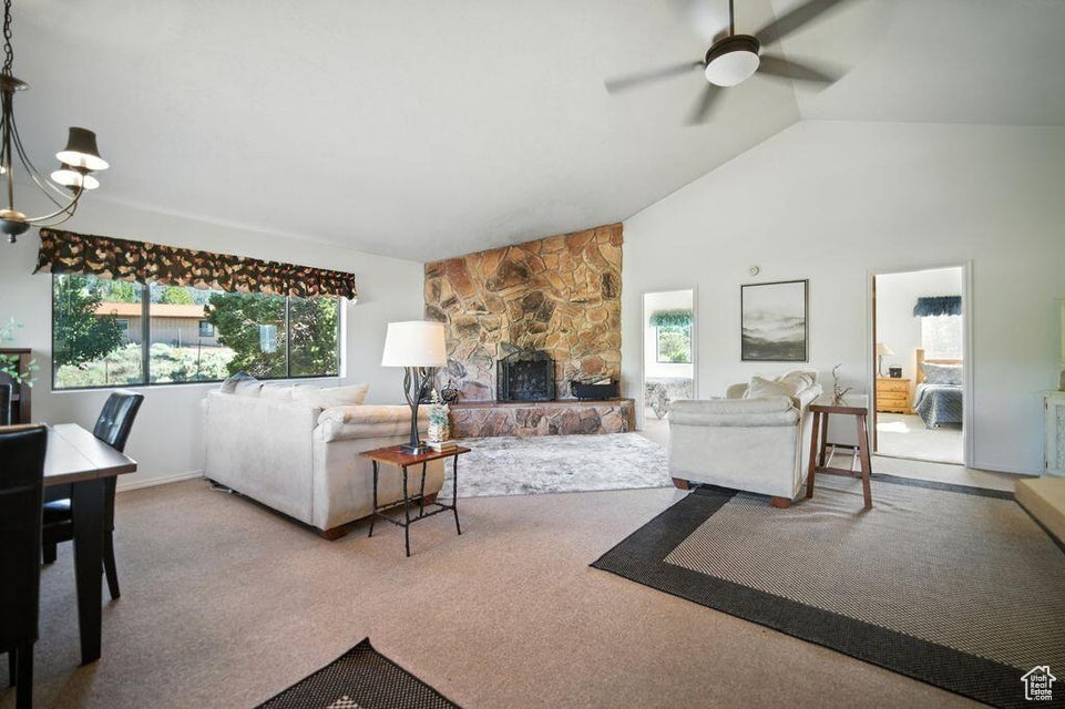 Living room featuring ceiling fan, carpet, a chandelier, a fireplace, and high vaulted ceiling
