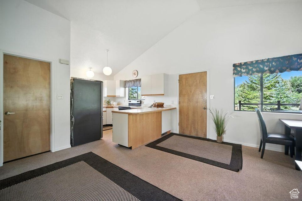 Kitchen featuring electric stove, freestanding refrigerator, high vaulted ceiling, a peninsula, and light countertops