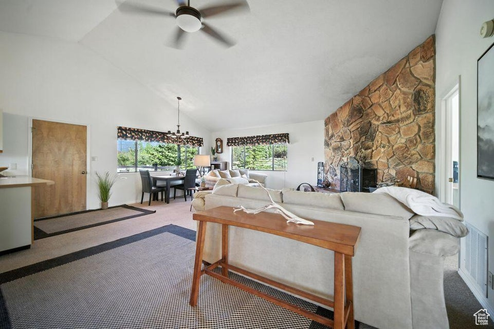Living area with ceiling fan, carpet floors, high vaulted ceiling, a fireplace, and a chandelier