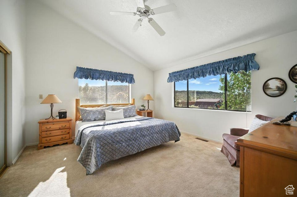 Bedroom featuring multiple windows, carpet floors, vaulted ceiling, and ceiling fan