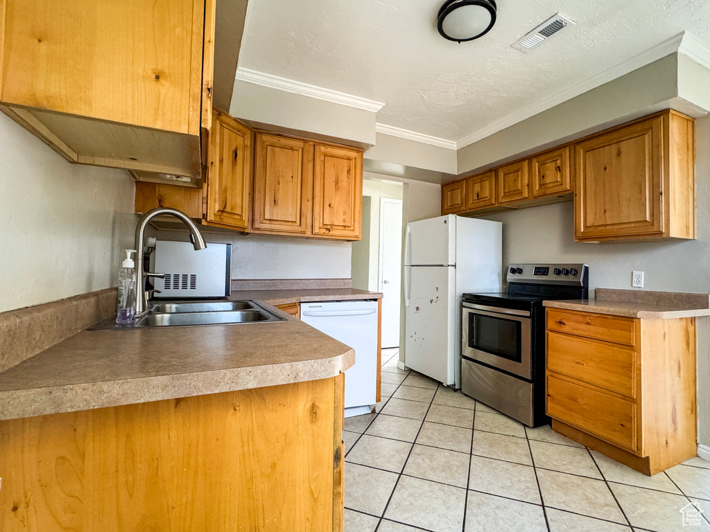 Kitchen with white appliances, light tile patterned floors, ornamental molding, and brown cabinetry