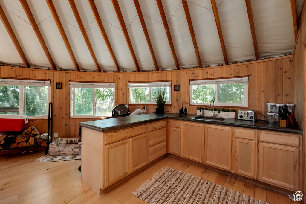Kitchen featuring light wood finished floors, wooden walls, dark countertops, a peninsula, and light brown cabinetry