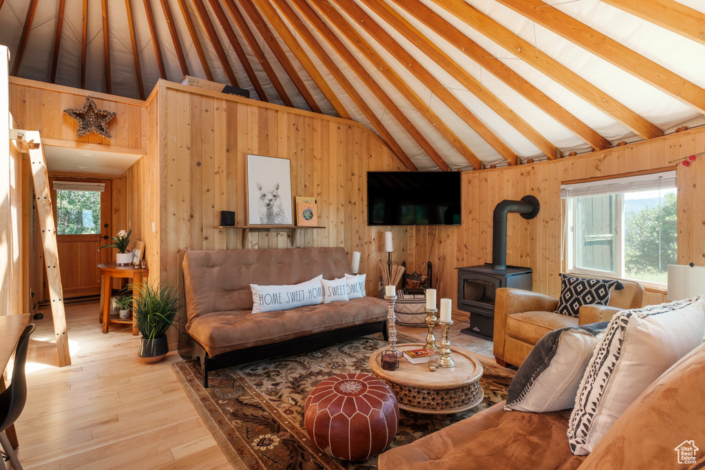 Living room featuring a wood stove, wood walls, hardwood / wood-style flooring, and high vaulted ceiling