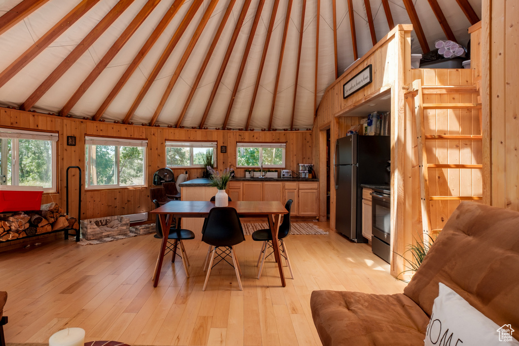 Dining room with beam ceiling, plenty of natural light, light wood-type flooring, wood walls, and high vaulted ceiling