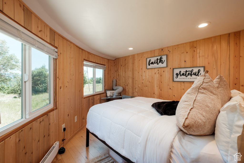 Bedroom with wood walls, light wood finished floors, recessed lighting, and a baseboard heating unit