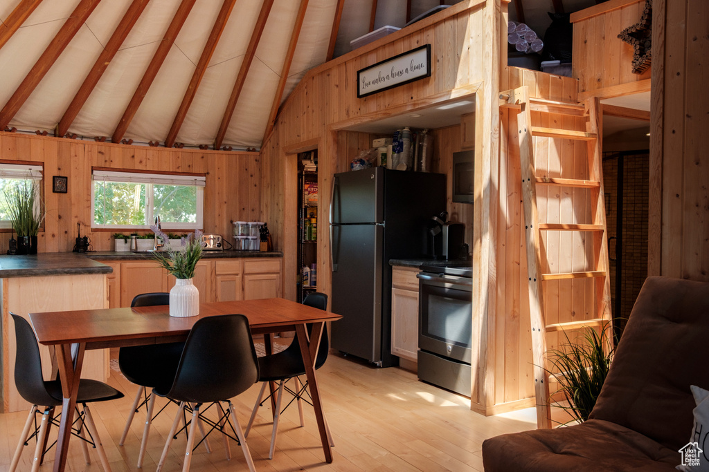 Kitchen featuring stainless steel electric stove, dark countertops, wooden walls, light wood-style floors, and freestanding refrigerator