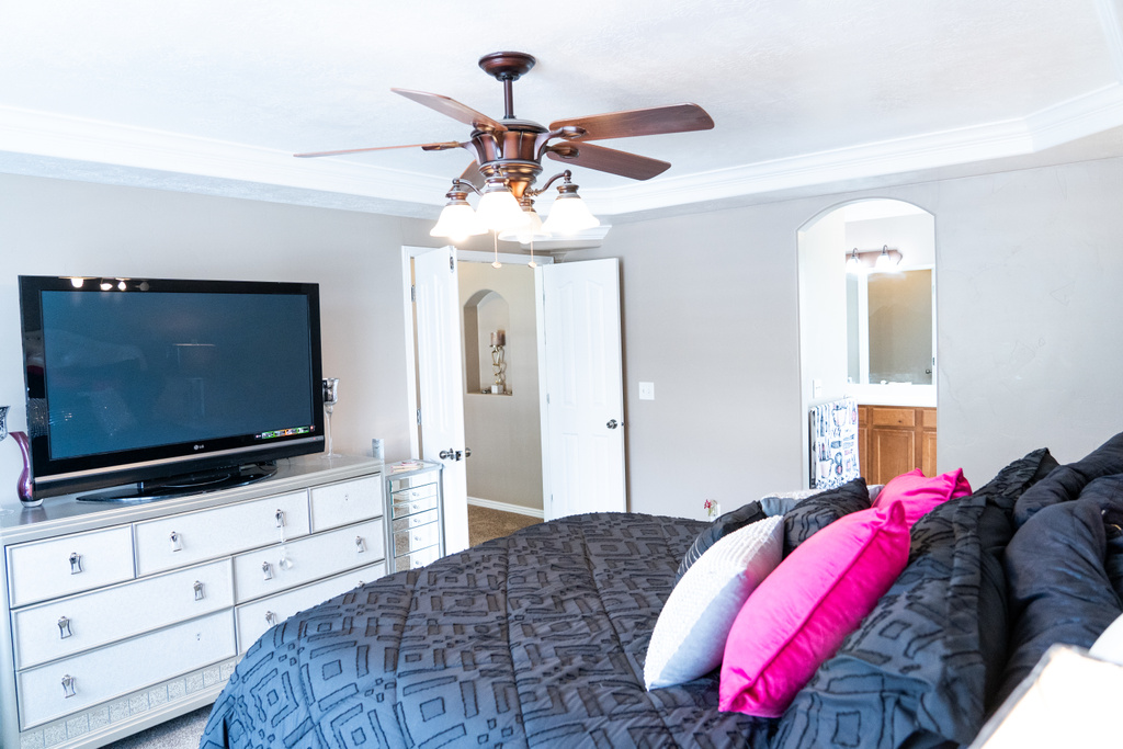 Bedroom with ornamental molding, arched walkways, carpet flooring, ensuite bath, and ceiling fan