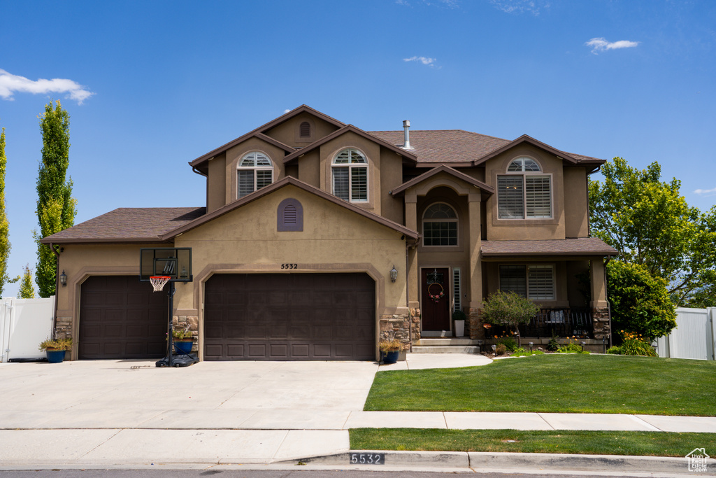 Traditional-style house with a garage, concrete driveway, stucco siding, stone siding, and covered porch