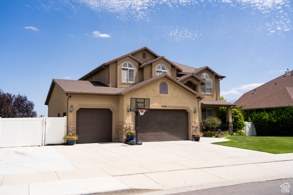 Traditional home featuring stucco siding, an attached garage, concrete driveway, stone siding, and a gate