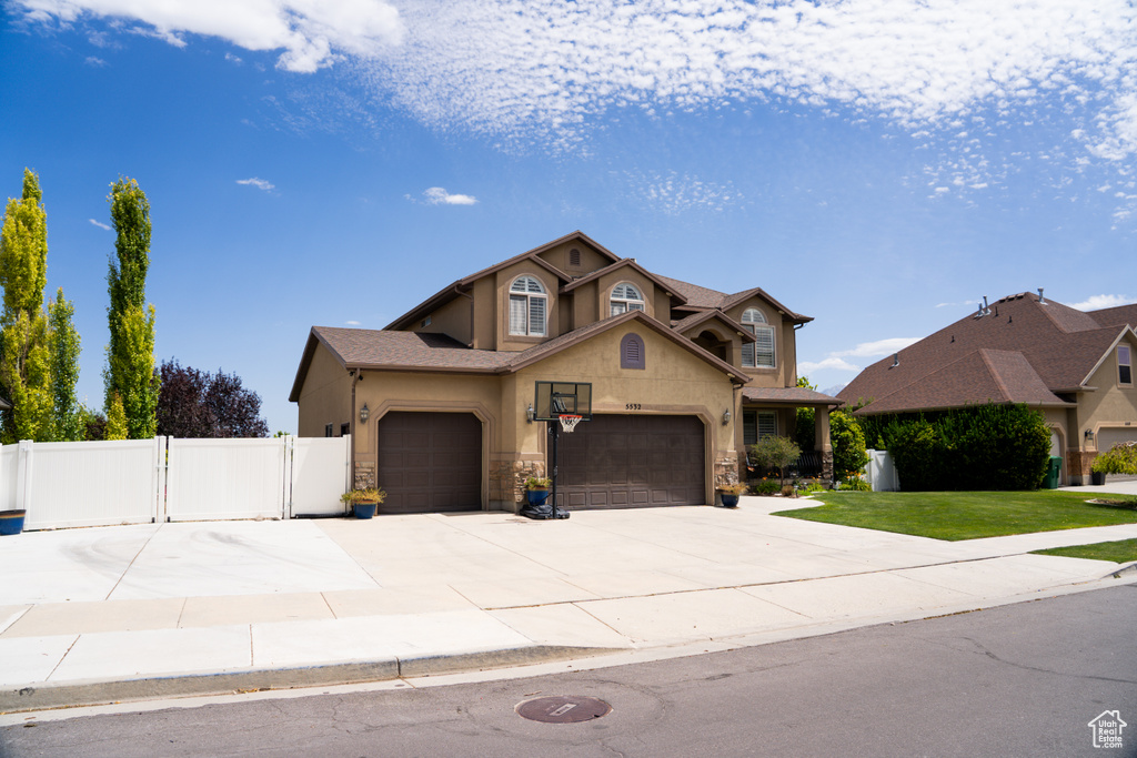 Traditional-style home with a gate, a garage, stucco siding, driveway, and stone siding