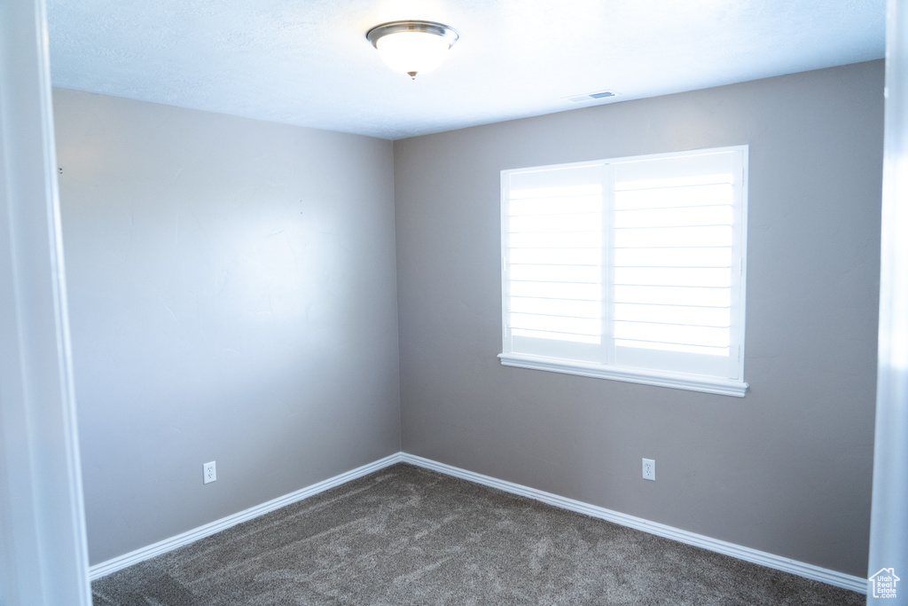 Unfurnished room featuring dark colored carpet and baseboards
