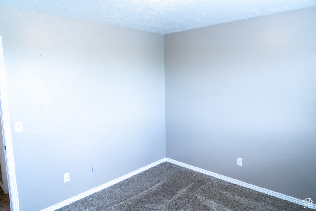 Spare room featuring dark colored carpet and a textured ceiling