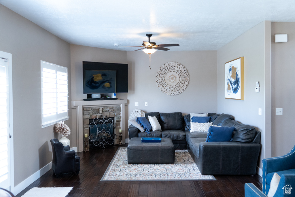 Living room with ceiling fan, dark wood finished floors, and a stone fireplace